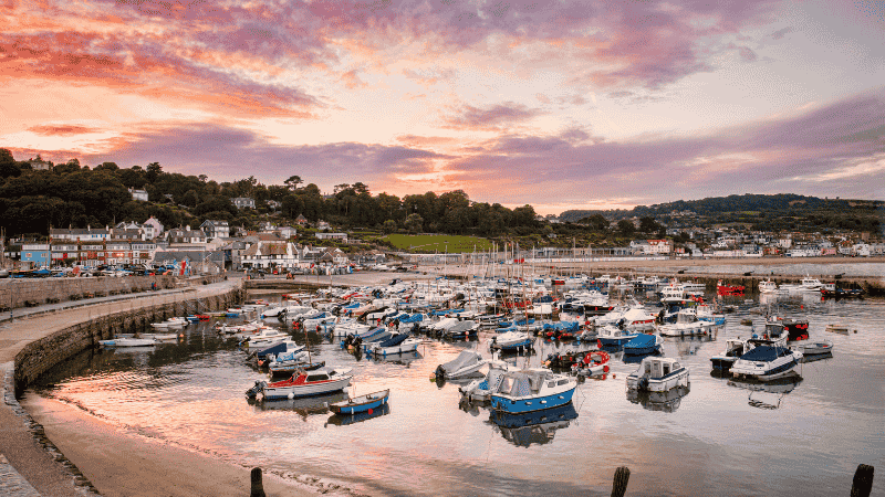 Boats moored in Lyme Regis harbor at sunset, a town in Dorset with rising house prices.