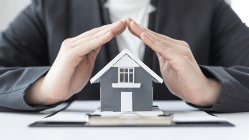 A property finance professional protecting a model house with their hands, symbolizing securing the best buy-to-let mortgage for a property investment.