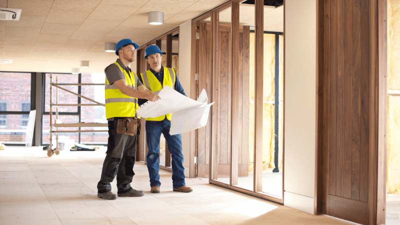 Two construction professionals in safety vests review blueprints for a commercial fit out project, a process often funded by fit out finance.
