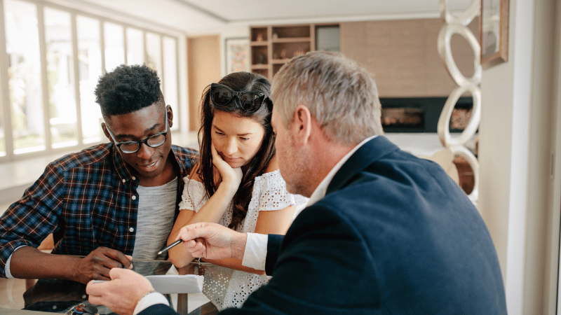 A professional mortgage broker explaining the details of a flexible mortgage document to a young couple.