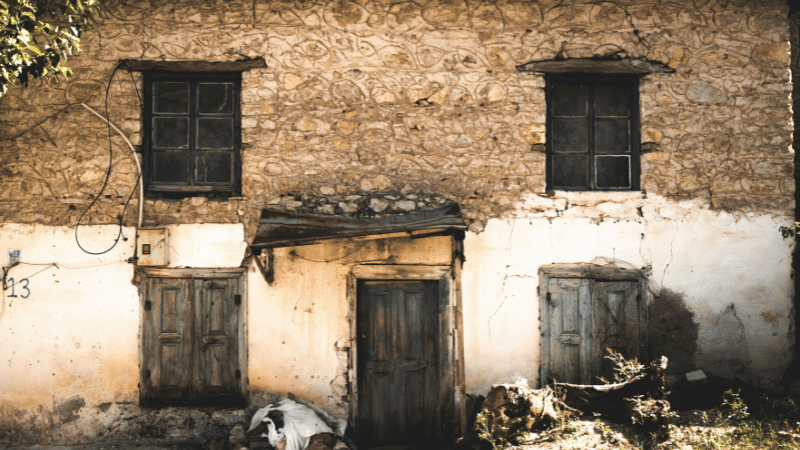 The weathered facade of a derelict stone house with old wooden doors and windows, representing an abandoned property with renovation potential.
