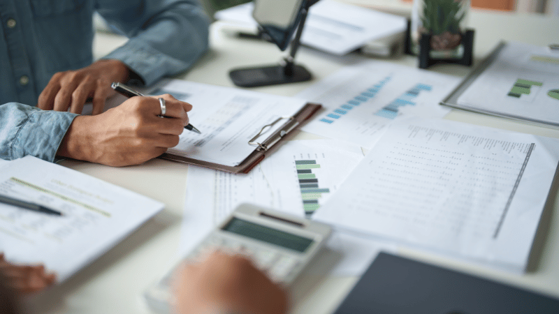 Two business professionals at a desk reviewing financial documents with charts and a calculator, planning how an invoice discounting facility can help their business grow.