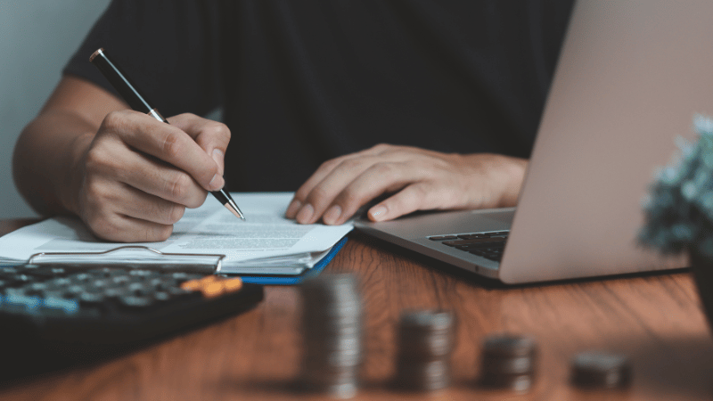 A business professional sits at a desk using a calculator and writing on financial documents, with a laptop nearby, representing leveraged finance planning.