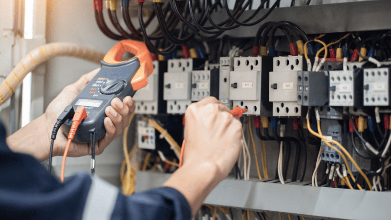A qualified electrician using a multimeter to test a complex electrical panel, representing the professional work funded by a merchant cash advance.