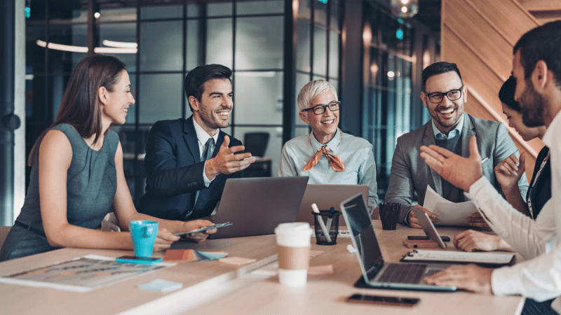 A team of smiling business professionals in a modern office meeting, discussing a growth strategy for their SaaS company after securing finance.