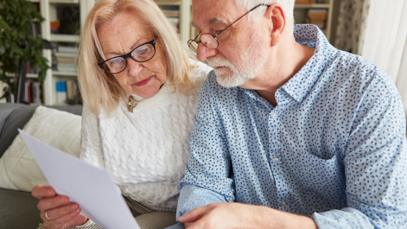 A smiling senior couple signing a pensioner mortgage agreement with a professional advisor.